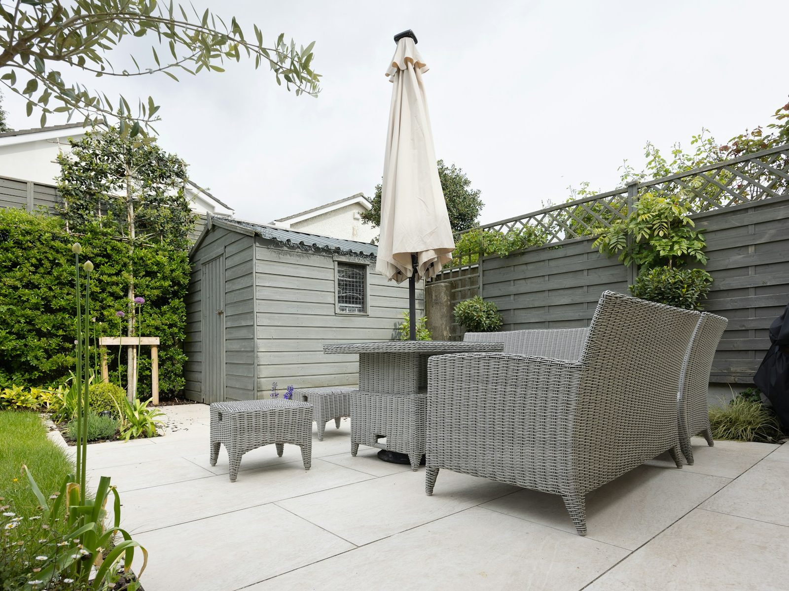 Terrasse aus großen Platten mit Lounge, Sonnenschirm, Gartenhaus und Sichtschutz